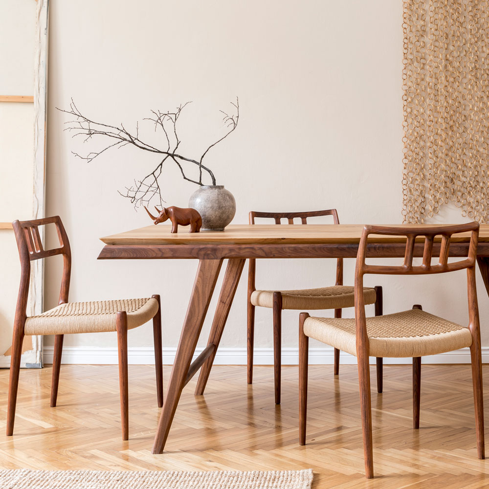 Ein minimalistischer Essbereich mit einem Holztisch, vier passenden Stühlen, einer Vase mit kahlen Zweigen und einer kleinen Elefantenfigur aus Holz. Die Einrichtung ist in neutralen Tönen und natürlichen Texturen gehalten.