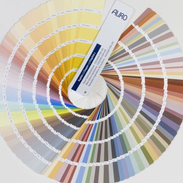 Ein AURO Farbfächer liegt geöffnet auf einem Tisch und präsentiert zahlreiche natürliche Farbtöne in harmonischer Anordnung.