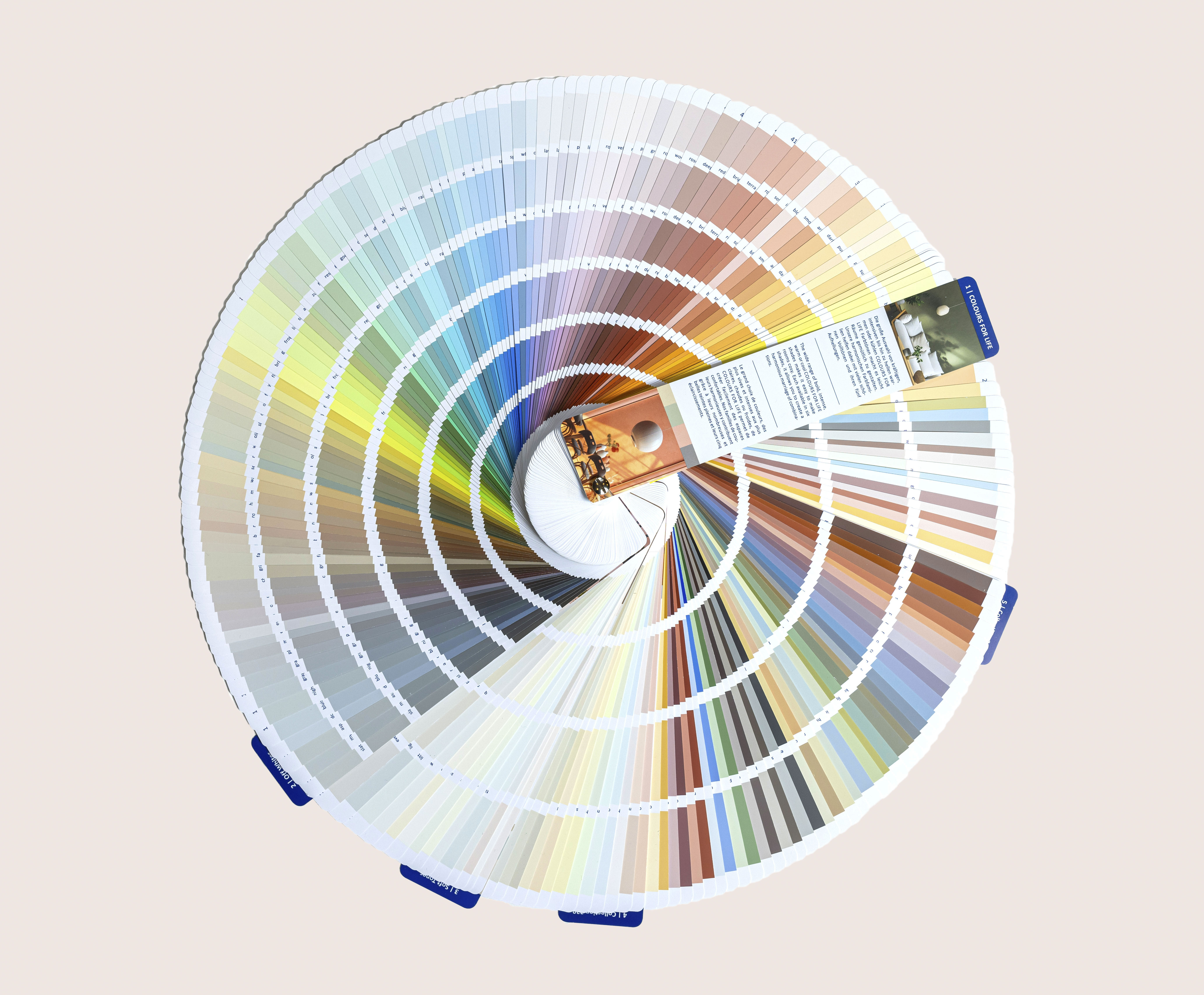 Ein runder Farbfächer mit spiralförmig aufgefächerten Farbmustern, der auf neutralem Hintergrund eine große Farbpalette von hellen bis zu dunklen Farbtönen zeigt.